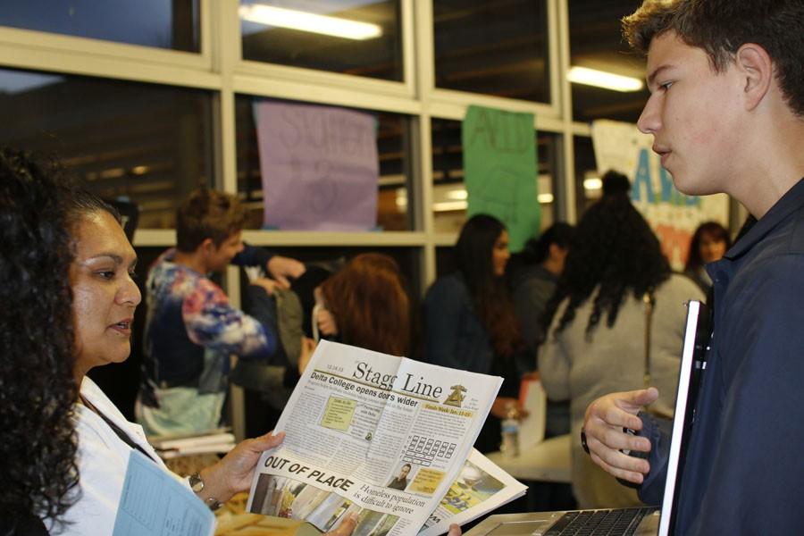 Junior Matteo Danforth, the opinion editor of the Stagg Line, holds a computer screen to display the website and informs a parent about the journalism program.