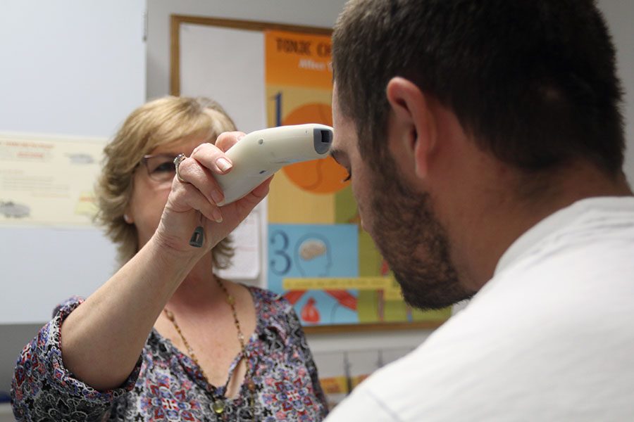 Healthy Start coordinator Judy Rauzi uses a thermal thermometer to take junior Arron Potts Collier’s temperature. 