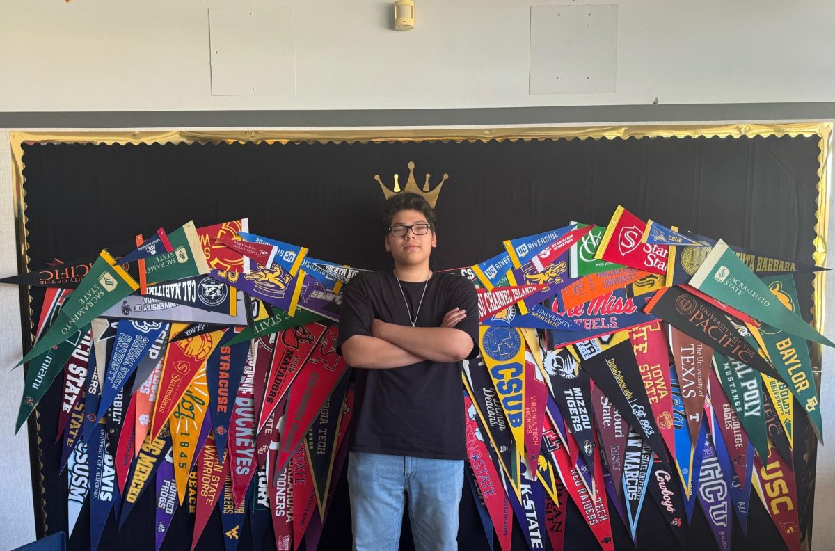 11th Grader Ruben Manabat stands in the center of a pair of wings in the Freshmen Center. The wings are made of different college pennants and symbolize how higher education can be the tool that takes you to new heights. (Jordan Martinez / Stagg Online)