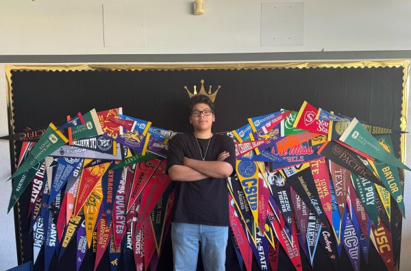 11th Grader Ruben Manabat stands in the center of a pair of wings in the Freshmen Center. The wings are made of different college pennants and symbolize how higher education can be the tool that takes you to new heights. (Jordan Martinez / Stagg Online)