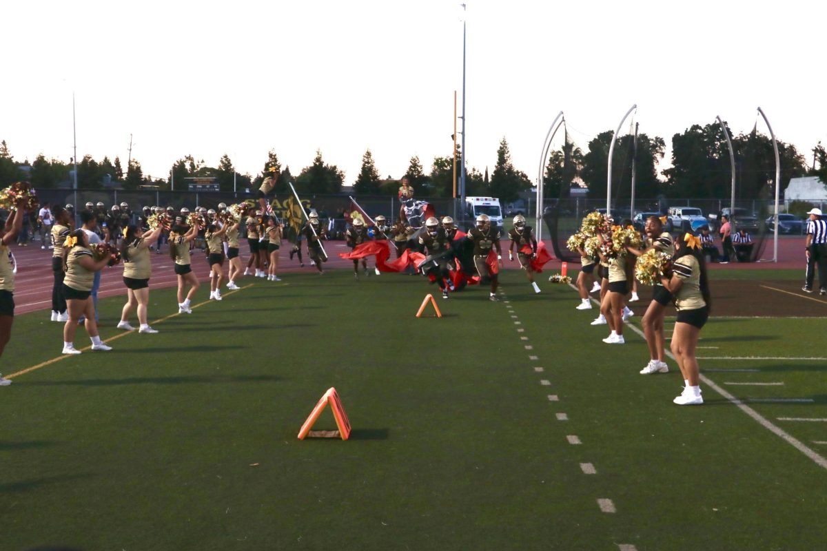 Varsity football players run through an introduction sign held by the varsity cheerleaders as others cheer them on from the sidelines, commencing the start of the Homecoming game.