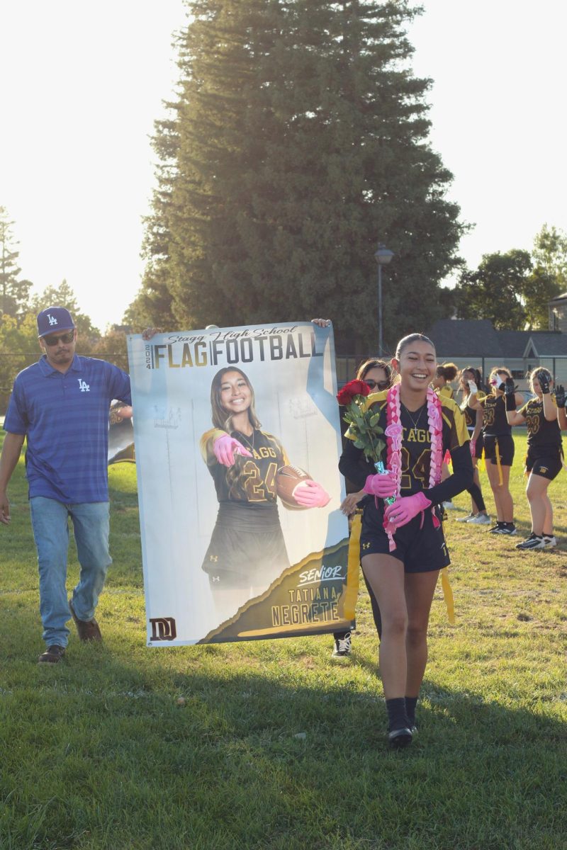 Cornerback Tatiana Negrete smiles cheerfully as she is cheered on by teammates. Her parents hold her banner as they walk behind her proudly. 