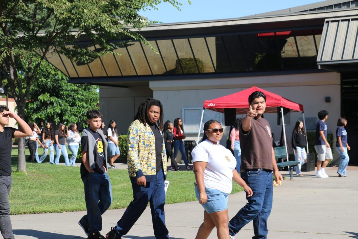 Two student leaders guide a group of freshmen on a campus tour. One points toward the theater while explaining its use and location.