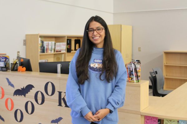 Evelyn Romero, the new library media assistant, standing in front of her desk. Behind her is the spot where students check out books.